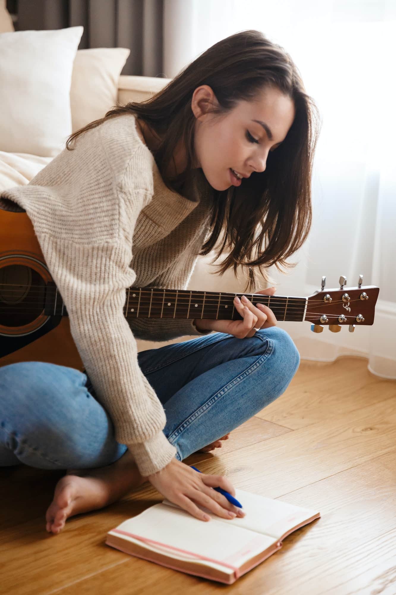 Image of focused beautiful woman playing guitar and composing song