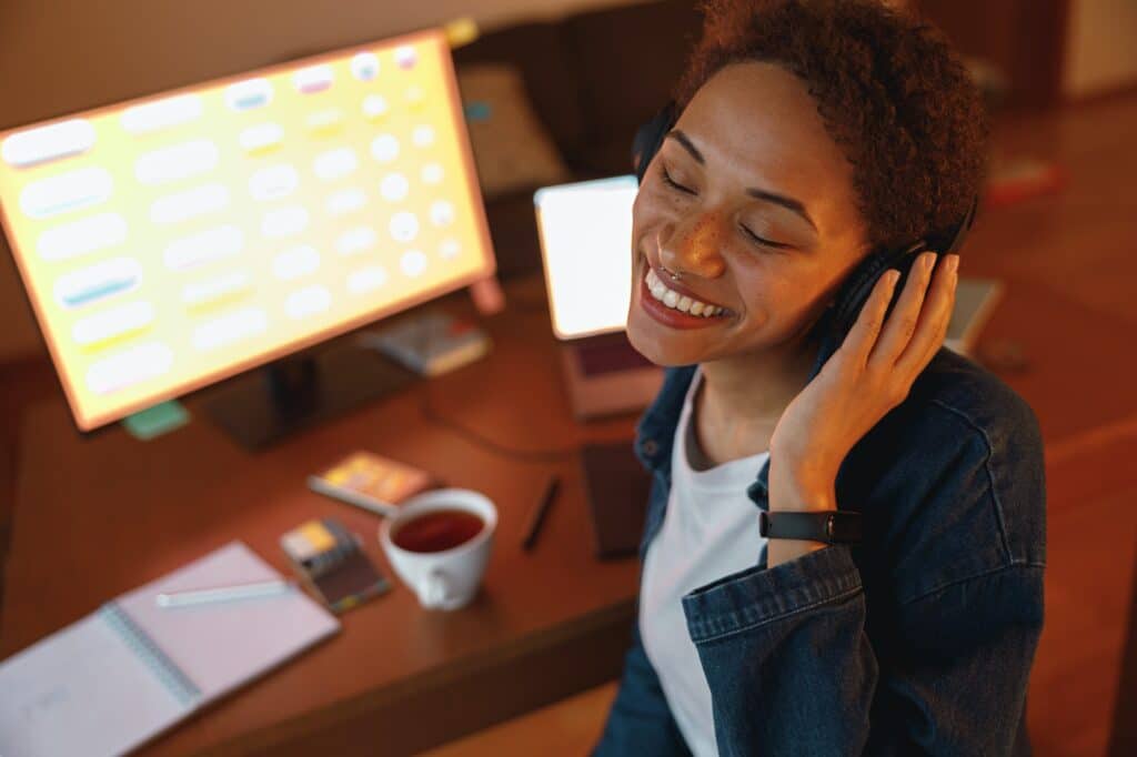 Smiling woman graphic designer enjoys listening music in headphones during break at home office